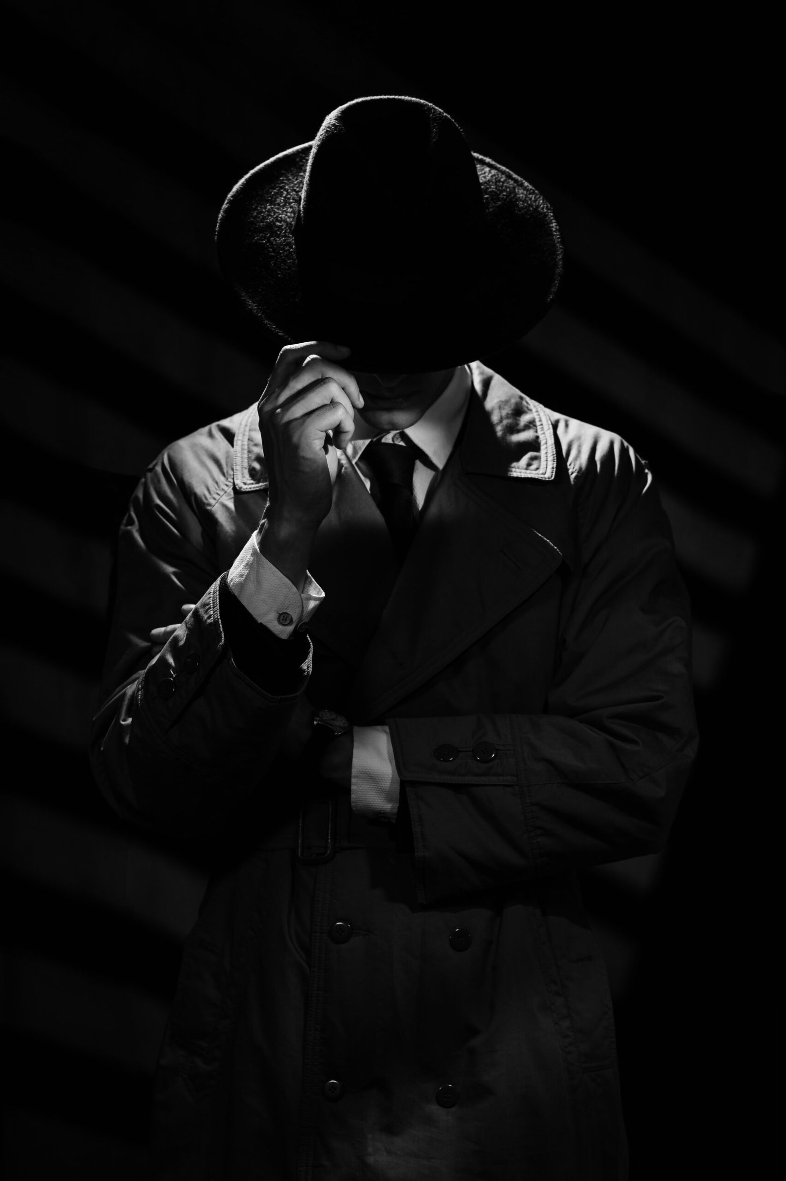 A dark silhouette of a man in a coat and hat in the noir style. A dramatic portrait in the style of detective films of the 1950s and 60s. The silhouette of a spy